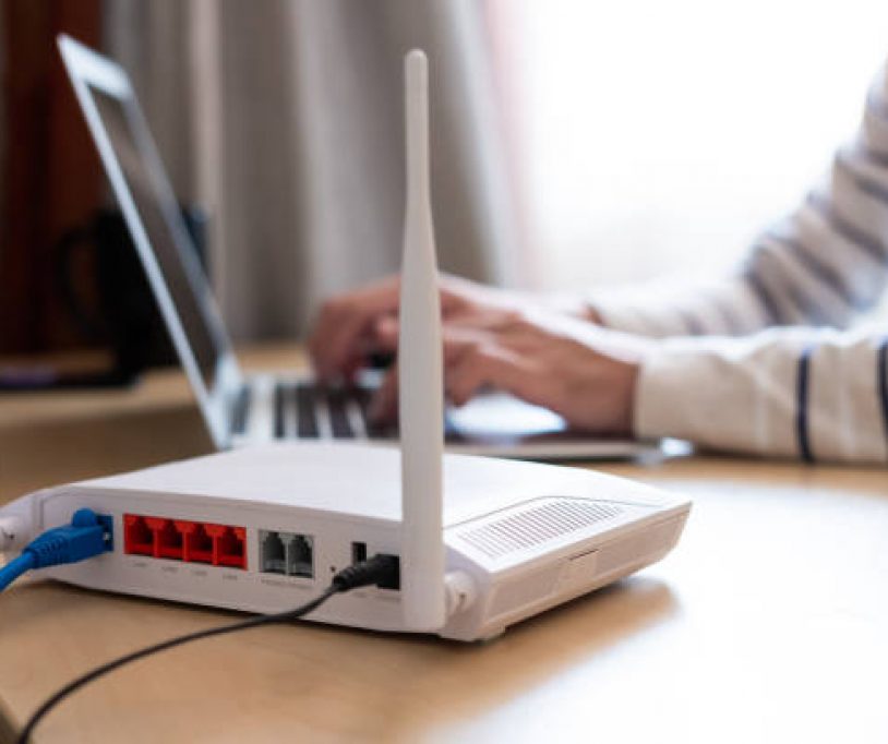 Selective focus at router. Internet router on working table with blurred man connect the cable at the background. Fast and high speed internet connection from fiber line with LAN cable connection.